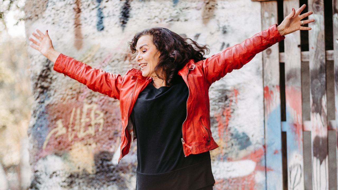 Katharina Maehrlein in roter Lederjacke mit ausgebreiteten Armen